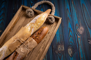 Two baguettes from wheat and buckwheat flour on a vintage tray on a blue wooden background.