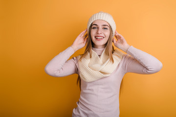 Obraz na płótnie Canvas Happy, young girl in hat and scarf posing in studio on orange background