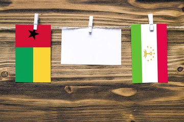 Hanging flags of Guinea Bissau and Tajikistan attached to rope with clothes pins with copy space on white note paper on wooden background.Diplomatic relations between countries.