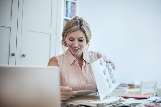Smiling woman with laptop working on fashion designs on table