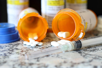 Precription bottles of pain pills and syringe on a granite countertop. 