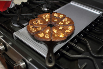Chocolate brownies with walnuts baked in a cast iron wedge pan, resting on the stove top in a home...