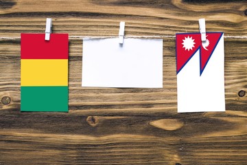 Hanging flags of Guinea and Nepal attached to rope with clothes pins with copy space on white note paper on wooden background.Diplomatic relations between countries.