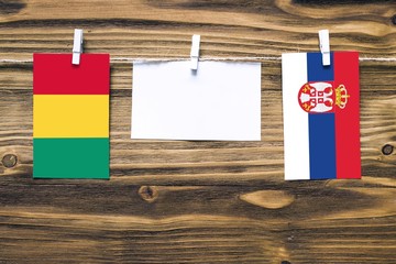 Hanging flags of Guinea and Serbia attached to rope with clothes pins with copy space on white note...