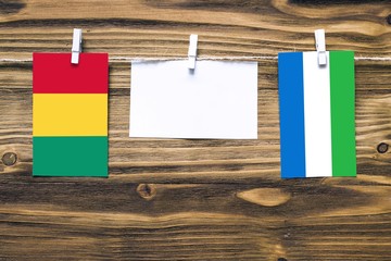 Hanging flags of Guinea and Sierra Leone attached to rope with clothes pins with copy space on white note paper on wooden background.Diplomatic relations between countries.