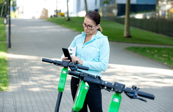 mature, woman scanning QR Code for activating rental electric scooter