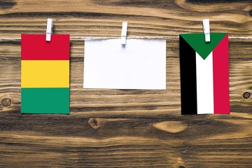 Hanging flags of Guinea and Sudan attached to rope with clothes pins with copy space on white note paper on wooden background.Diplomatic relations between countries.