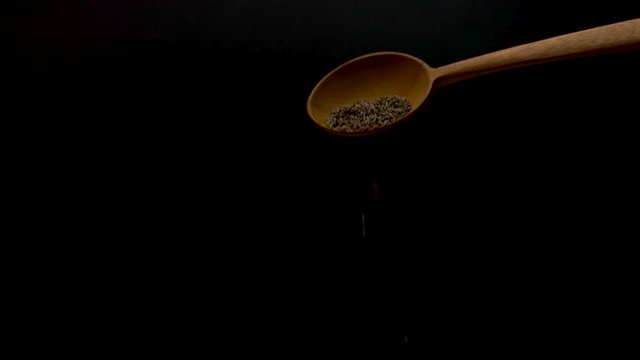 Cumin poured from a wooden spoon rapidly