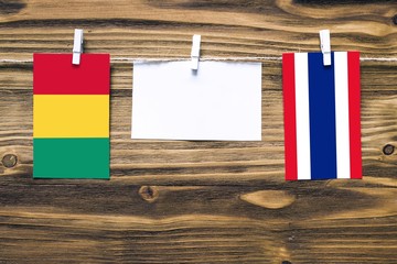 Hanging flags of Guinea and Thailand attached to rope with clothes pins with copy space on white note paper on wooden background.Diplomatic relations between countries.