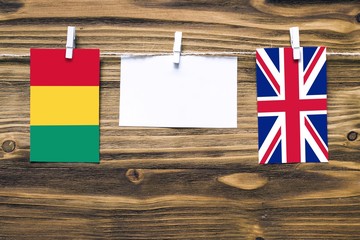 Hanging flags of Guinea and United Kingdom attached to rope with clothes pins with copy space on white note paper on wooden background.Diplomatic relations between countries.