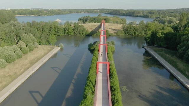Modern architectural complex in the city of Cergy on the Oise River, France. Aerial shot of a conceptual bridge with red arches. Beautiful play of light and shadow
