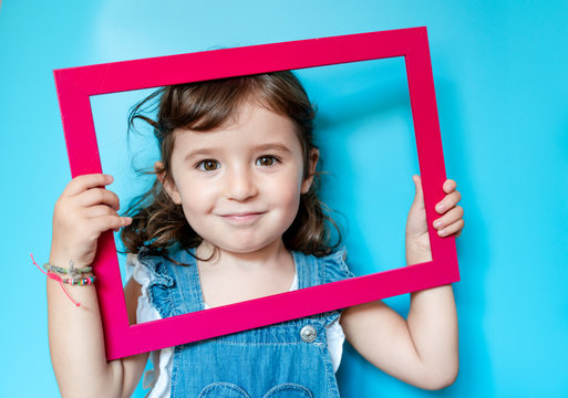 Portrait of cute little girl holding a picture frame on blue background