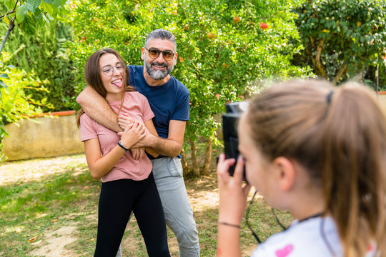 Girl taking a picture of happy father with daughter in garden