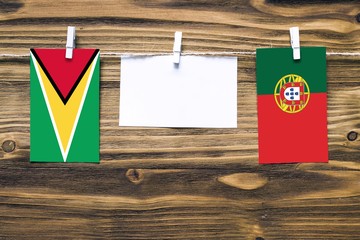 Hanging flags of Guyana and Portugal attached to rope with clothes pins with copy space on white note paper on wooden background.Diplomatic relations between countries.