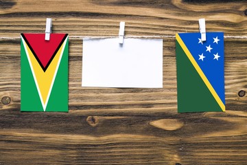 Hanging flags of Guyana and Solomon Islands attached to rope with clothes pins with copy space on...