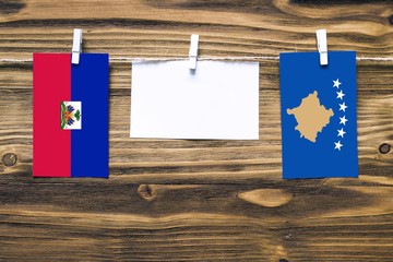 Hanging flags of Haiti and Kosovo attached to rope with clothes pins with copy space on white note...