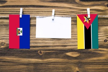 Hanging flags of Haiti and Mozambique attached to rope with clothes pins with copy space on white...