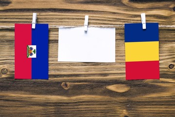 Hanging flags of Haiti and Romania attached to rope with clothes pins with copy space on white note...