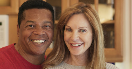 African American husband and Caucasian wife in kitchen looking at camera