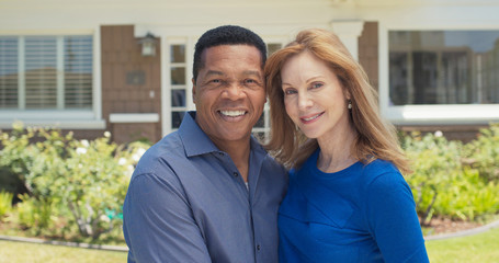 Portrait of older couple smiling in front of their home