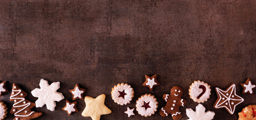 Assorment of Christmas cookies and sweets. Overhead view border banner over a dark stone background with copy space. Holiday baking concept.