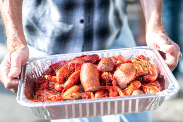 Closeup of red lobsters and crawfish seafood with hands holding tray of red shellfish in New...