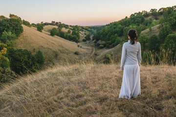 Young woman in white clothing standing and watching autumn evening sky over the hills of Deliblatska pescara (Deliblato sands) in Serbia