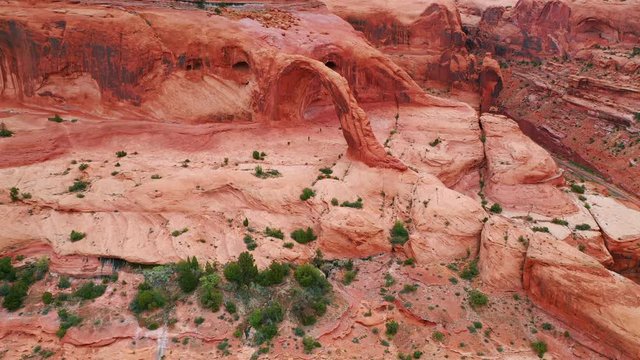Aerial: Drone approaching hikers below natural arch on rocky mountain in desert - Moab, Utah