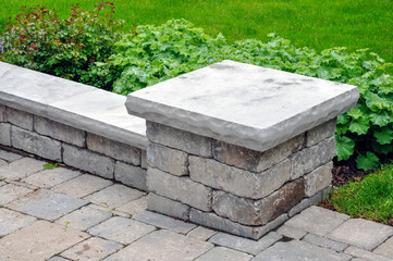 A seat wall with pillars and natural stone coping helps define a tumbled paver driveway and is a...