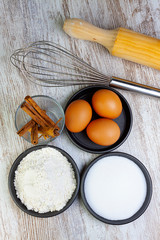 INGREDIENTS AND KITCHEN UTENSILS FOR PASTRY. FLOUR, SUGAR, EGGS AND CINNAMON NEXT TO WOOD AND ROLLER WOOD