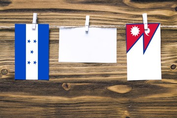 Hanging flags of Honduras and Nepal attached to rope with clothes pins with copy space on white note paper on wooden background.Diplomatic relations between countries.