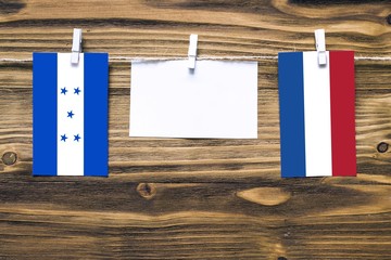 Hanging flags of Honduras and Netherlands attached to rope with clothes pins with copy space on white note paper on wooden background.Diplomatic relations between countries.