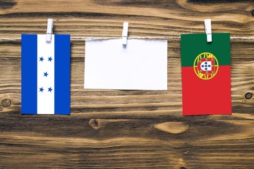 Hanging flags of Honduras and Portugal attached to rope with clothes pins with copy space on white note paper on wooden background.Diplomatic relations between countries.