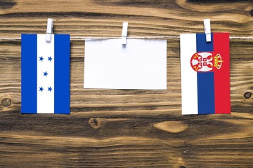 Hanging flags of Honduras and Serbia attached to rope with clothes pins with copy space on white note paper on wooden background.Diplomatic relations between countries.