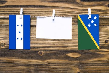 Hanging flags of Honduras and Solomon Islands attached to rope with clothes pins with copy space on white note paper on wooden background.Diplomatic relations between countries.