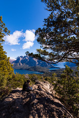 Young couple resting on the rocks beneath the shadow of a coihue tree against Andes range and...