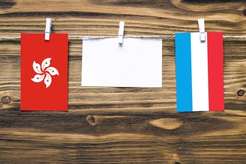 Hanging flags of Hong Kong and Luxembourg attached to rope with clothes pins with copy space on white note paper on wooden background.Diplomatic relations between countries.