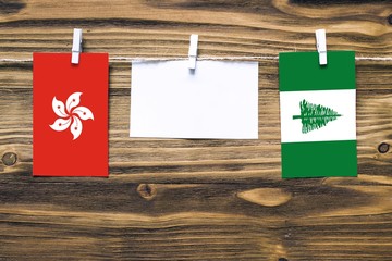 Hanging flags of Hong Kong and Norfolk Island attached to rope with clothes pins with copy space on white note paper on wooden background.Diplomatic relations between countries.