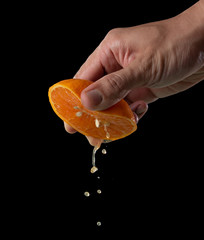 Hand squeeze orange slice with orange juice on black background