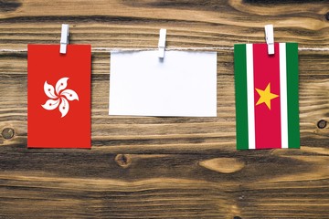 Hanging flags of Hong Kong and Suriname attached to rope with clothes pins with copy space on white note paper on wooden background.Diplomatic relations between countries.