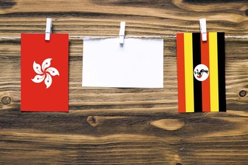 Hanging flags of Hong Kong and Uganda attached to rope with clothes pins with copy space on white note paper on wooden background.Diplomatic relations between countries.