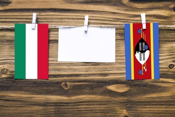 Hanging flags of Hungary and Swaziland attached to rope with clothes pins with copy space on white note paper on wooden background.Diplomatic relations between countries.