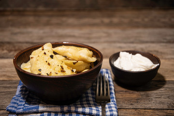 Dumplings with potatoes and onion frying in a ceramic bowl, napkin, fork and pottery with sour cream.