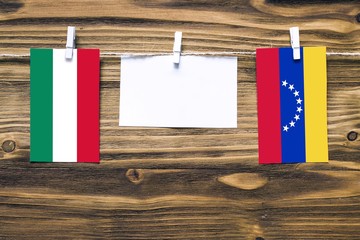 Hanging flags of Hungary and Venezuela attached to rope with clothes pins with copy space on white note paper on wooden background.Diplomatic relations between countries.