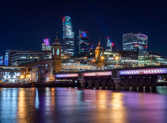Skyline of London at night including illuminated bridge over Thames river and city of london in the background