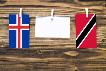 Hanging flags of Iceland and Trinidad And Tobago attached to rope with clothes pins with copy space on white note paper on wooden background.Diplomatic relations between countries.