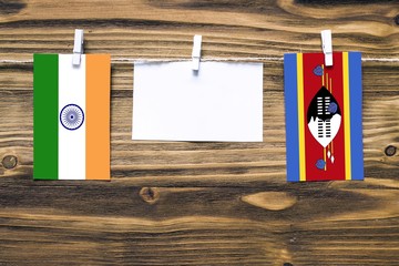 Hanging flags of India and Swaziland attached to rope with clothes pins with copy space on white note paper on wooden background.Diplomatic relations between countries.
