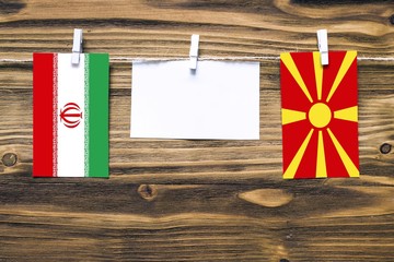 Hanging flags of Iran and Macedonia attached to rope with clothes pins with copy space on white...