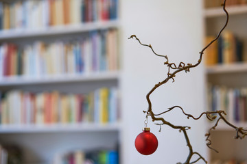 Close up of red christmas ball in front of unsharp book shelf in loft