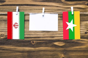 Hanging flags of Iran and Myanmar attached to rope with clothes pins with copy space on white note paper on wooden background.Diplomatic relations between countries.